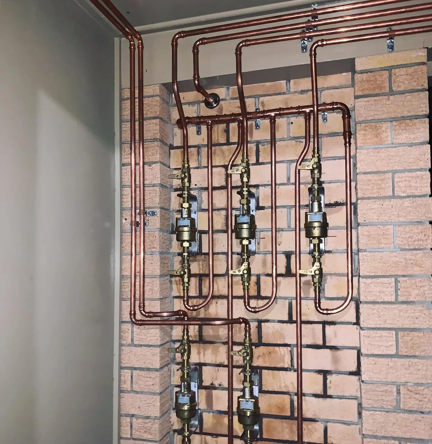 Copper pipe manifold with a row of isolation valves neatly run across a brick wall